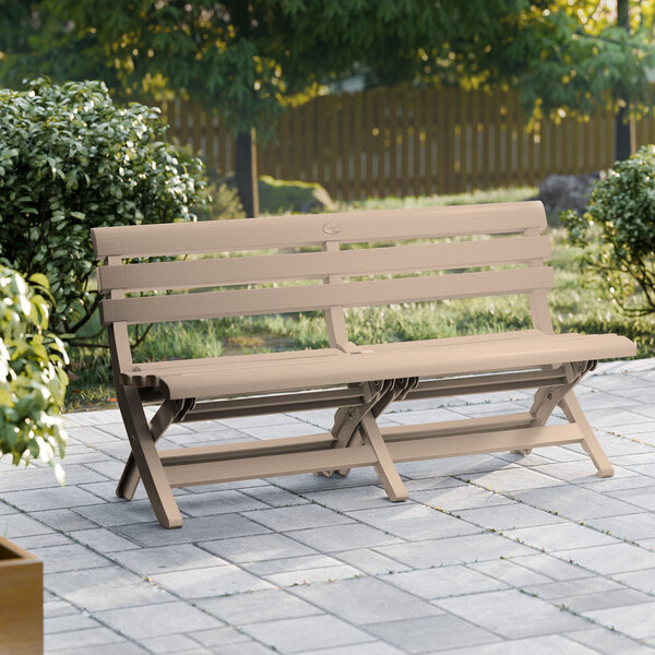 A Grosfillex French Taupe faux wood bench on a stone patio.