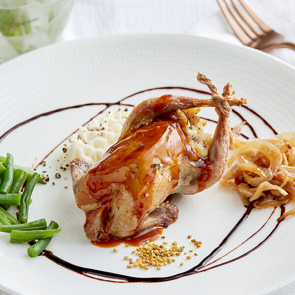 A white plate topped with a Manchester Farms whole quail and green beans with a fork on the side.
