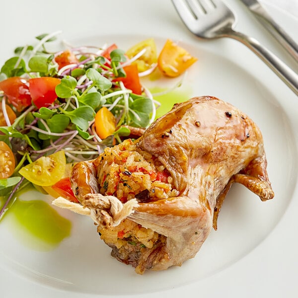 A plate of food with a whole quail, a side of salad, a fork, and a knife.