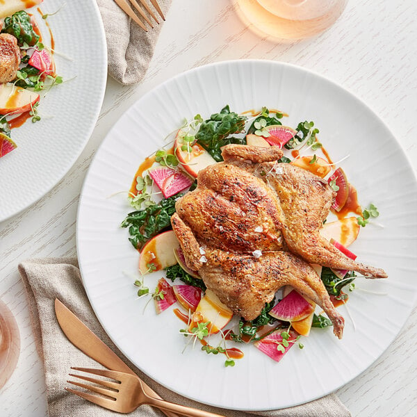 A plate of fresh butterfly cut quail with vegetables and a fork and knife on a table.