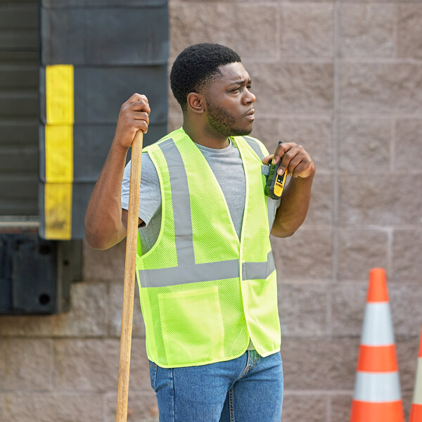 A man in a lime Ergodyne safety vest holding a tool.