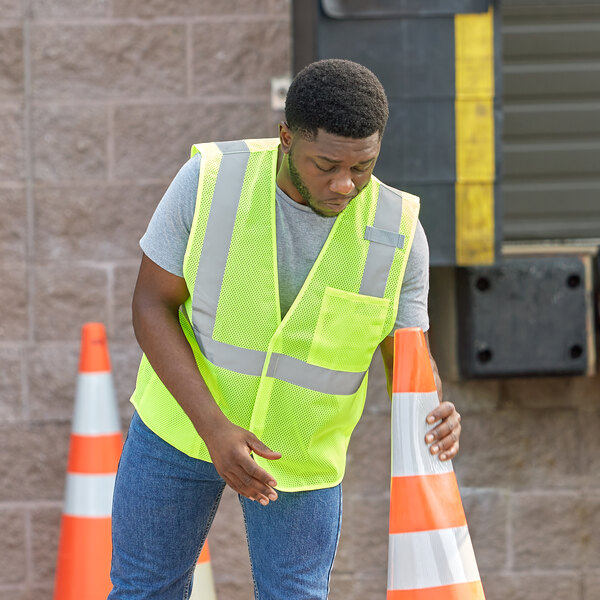 A man in a safety vest leaning on a traffic cone.