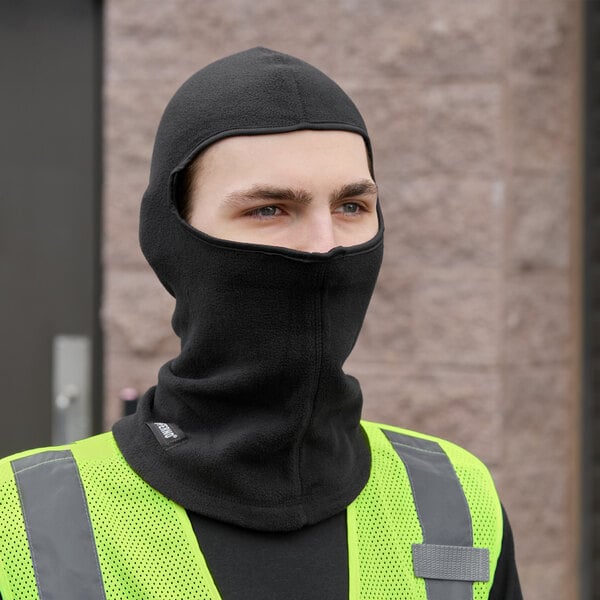 A man wearing a black balaclava and yellow reflective vest.