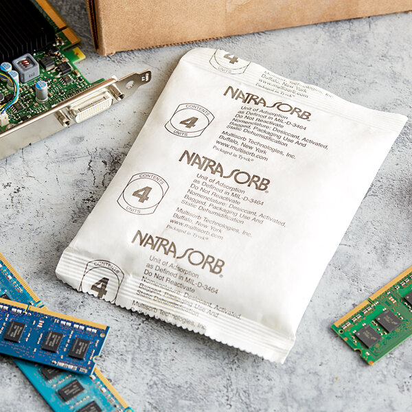 A white Multisorb silica packet with black text next to computer chips and a blue circuit board.