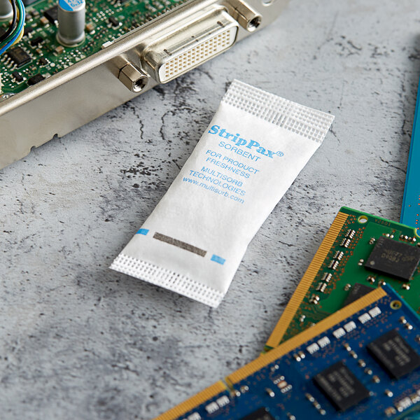 A white Multisorb StripPax packet with blue text sitting next to electronic components.