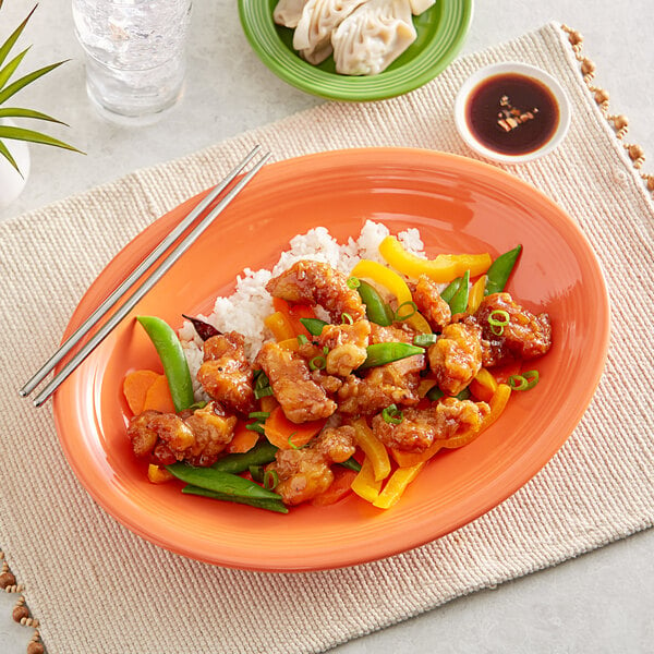 An Acopa Valencia Orange oval stoneware platter with a plate of food on a table.