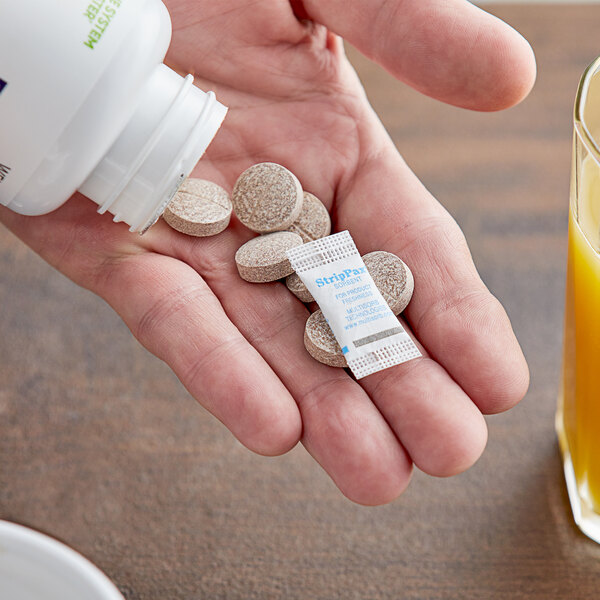 A hand holding a white bottle and several Multisorb StripPax desiccant packets with pills.