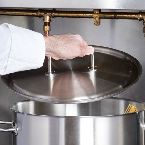 A chef using a Vollrath stainless steel lid to cover a large pot.