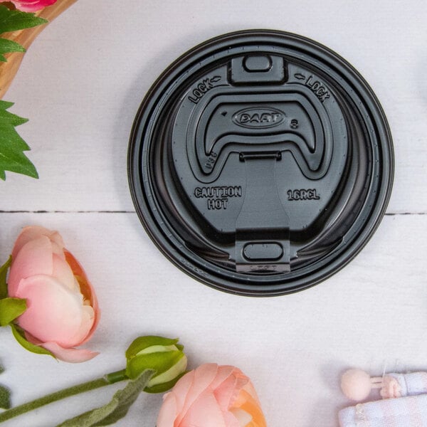 A Dart black lid with reclosable tab on a white surface next to pink flowers.