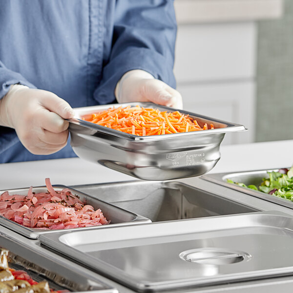 A person in a blue uniform using a Vollrath stainless steel steam table pan to serve shredded carrots.