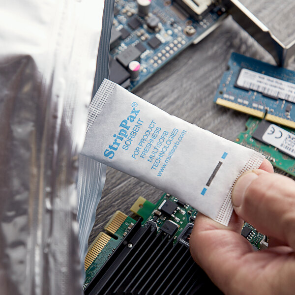 A person holding a Multisorb StripPax desiccant packet over a circuit board.