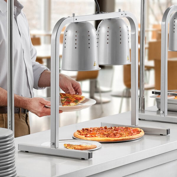 A man using a ServIt pass through heat lamp to serve pizza on a countertop.