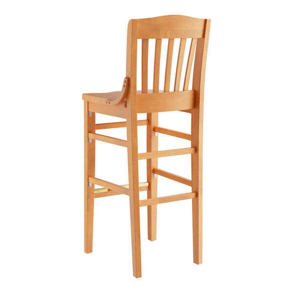A Lancaster Table & Seating wooden school house bar stool with a backrest.