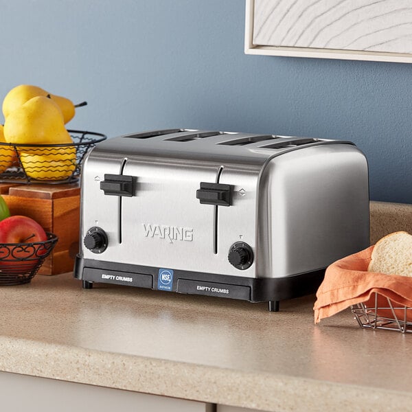 A silver Waring commercial toaster with black knobs on a counter with four slices of toast.