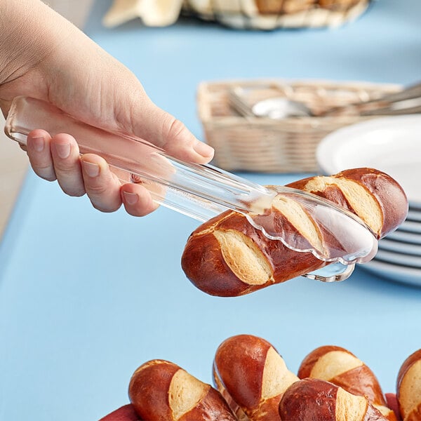 A hand using clear plastic tongs to pick up a pretzel