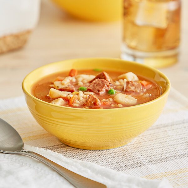 A yellow Acopa Capri stoneware bowl filled with soup with meat and vegetables on a table.