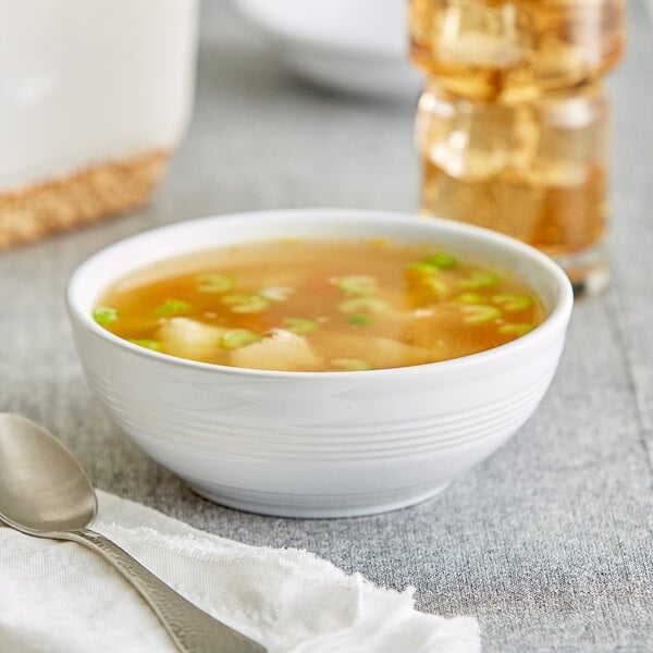 A close-up of a bowl of soup with green onions and a spoon on a white surface.