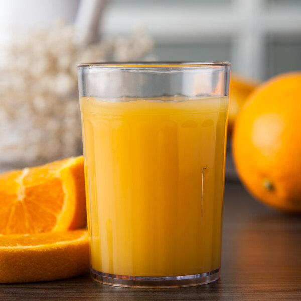 A Carlisle clear plastic tumbler filled with orange juice with a slice of orange on the rim.