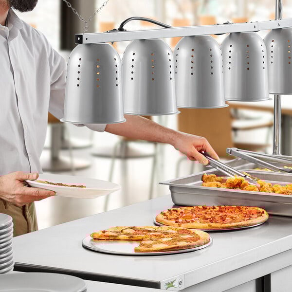 A man in a white shirt and black hat using a ServIt hanging heat lamp to serve food.