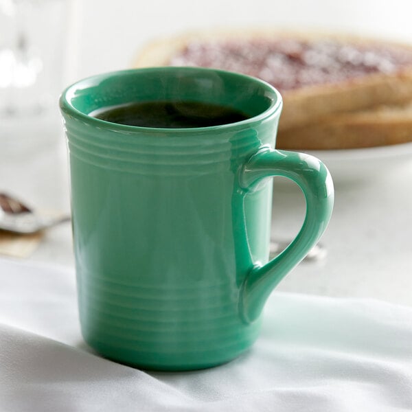 A close-up of a Tuxton Cilantro green mug with a handle on a white cloth.