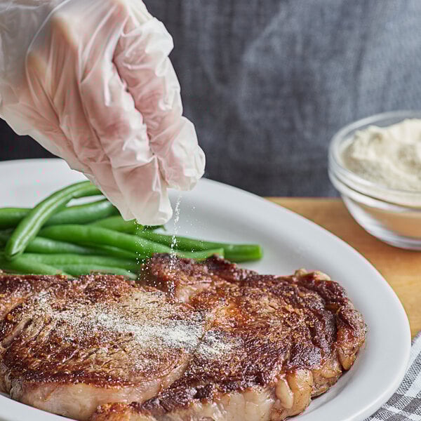 A gloved hand sprinkling Regal Onion Salt on a piece of meat with green beans.