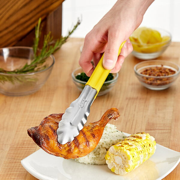 A person using Choice yellow handled stainless steel scalloped tongs to serve herbs into a bowl.