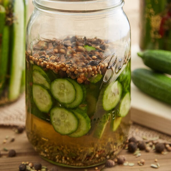A jar of pickles and cucumbers with spices and herbs.