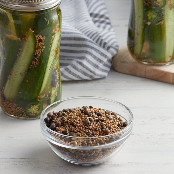 A bowl of Regal Old Fashioned Pickling Spice on a table with jars of pickles and cucumbers.