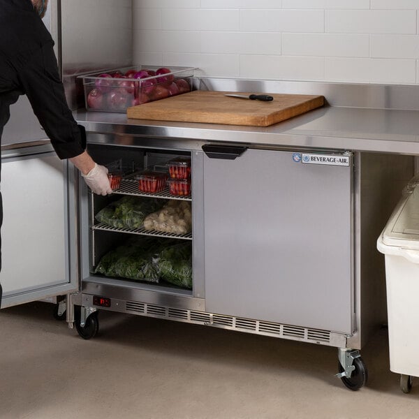 A man in a kitchen putting food into a Beverage-Air undercounter refrigerator.