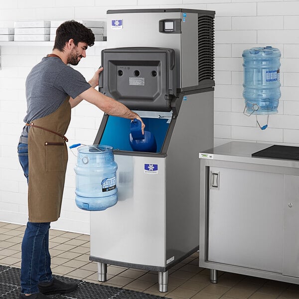 A man filling a blue container with ice from a Manitowoc air cooled ice machine.