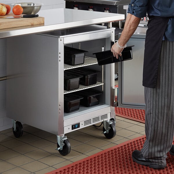 A man opening a Beverage-Air undercounter freezer filled with food trays.