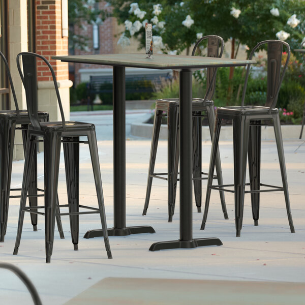 A Lancaster Table & Seating rectangular bar height table with textured metal finish and end base plates on a patio.