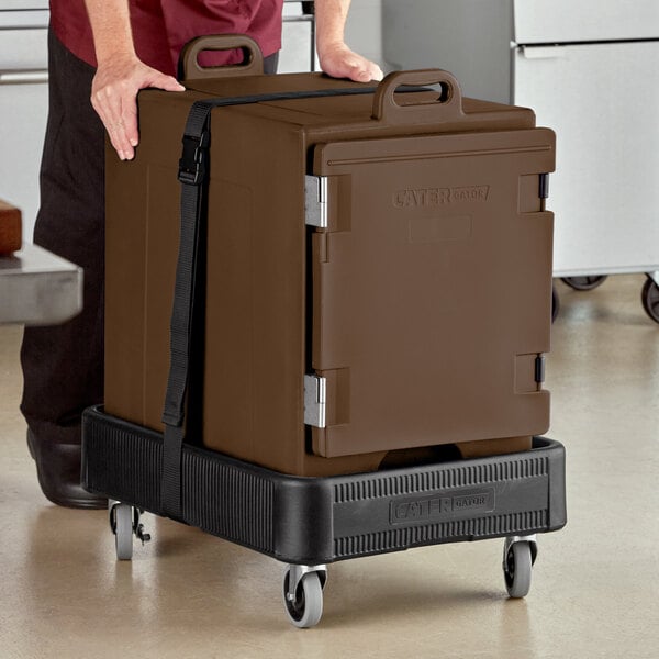 A man pushing a brown CaterGator front loading food pan carrier with wheels.