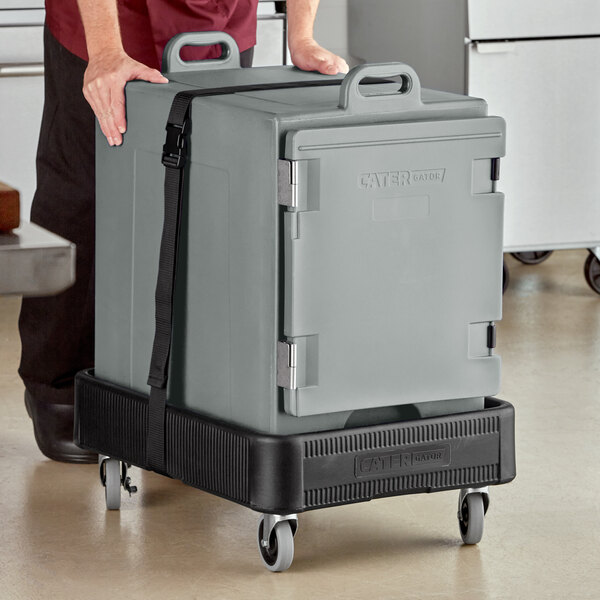 A man pushing a large grey CaterGator cooler on a cart.