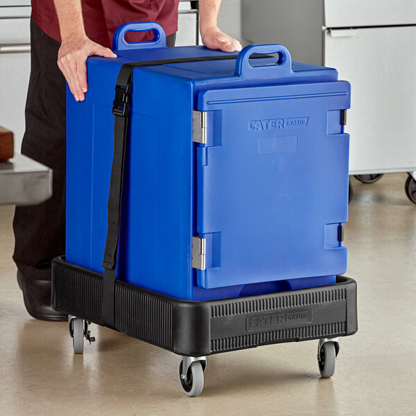 A man pushing a large blue CaterGator food pan carrier on a black dolly with a strap.