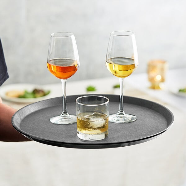 A person holding a Choice gray non-skid serving tray with glasses of white wine and ice.