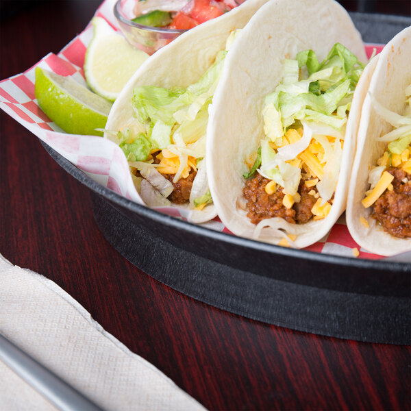 An oval deli server filled with tacos, a lime wedge, and a knife on a table.