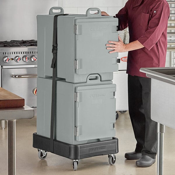 A man in a chef's uniform holding a stack of grey CaterGator pan carriers.