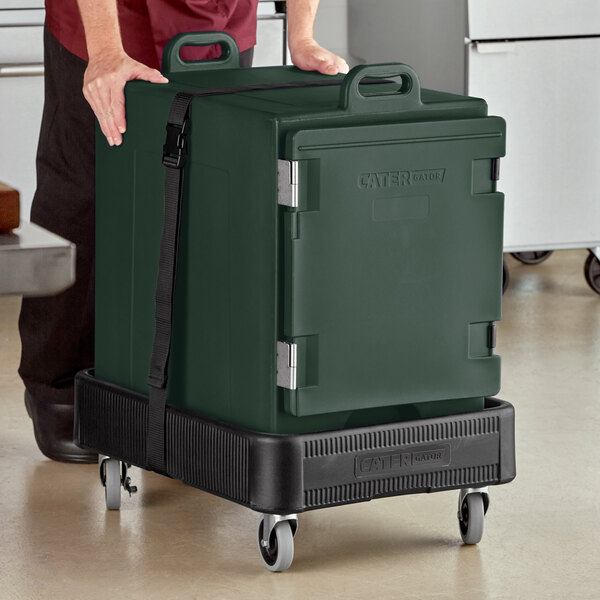 A man pushing a large green CaterGator food pan carrier on wheels.