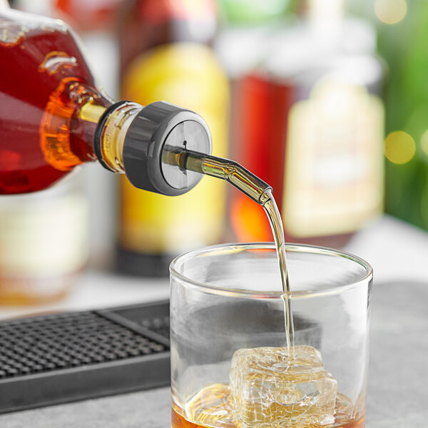 A person using a Choice Smoke Free Flow Whiskey Pourer to pour a drink into a glass.