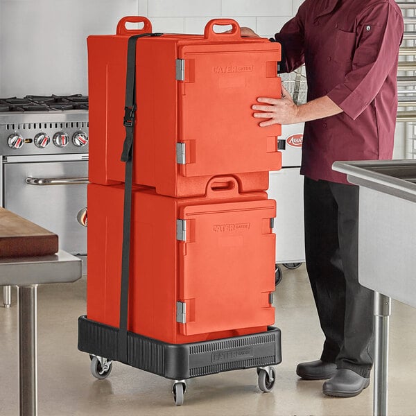 A man in a chef's uniform holding two red CaterGator pan carriers.