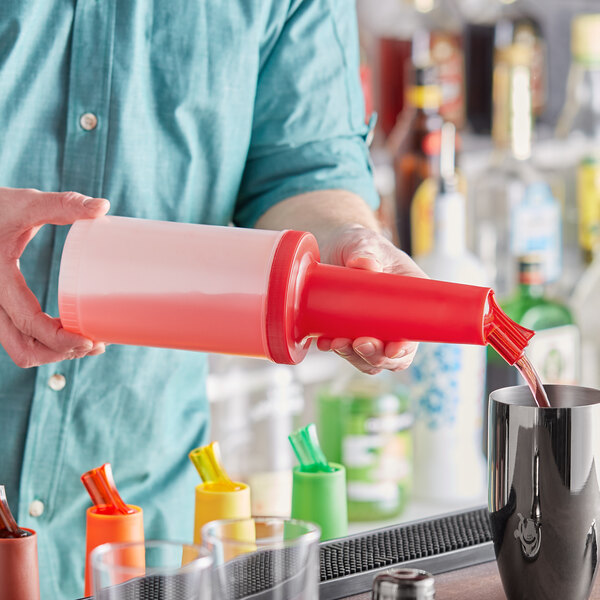 A person pouring liquid from a red Choice pour bottle into a cup.
