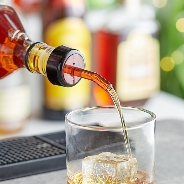 A Choice red free flow whiskey pourer with black collar pouring whiskey into a glass with ice.