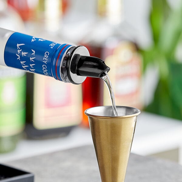 A person using a Choice black free flow liquor pourer to fill a shot glass on a table in a cocktail bar.