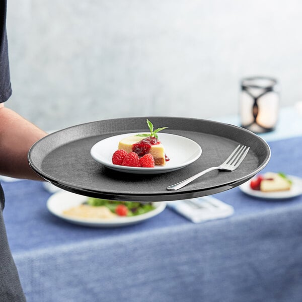 A person holding a Choice gray non-skid serving tray with a plate of dessert with raspberries and a fork.