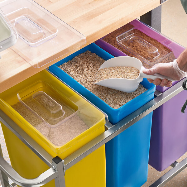 A person using a scoop to fill a white bowl with cereal from a purple Baker's Mark ingredient bin.