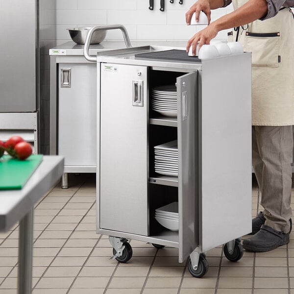 A man putting plates on a Regency stainless steel utility cart with enclosed shelves.
