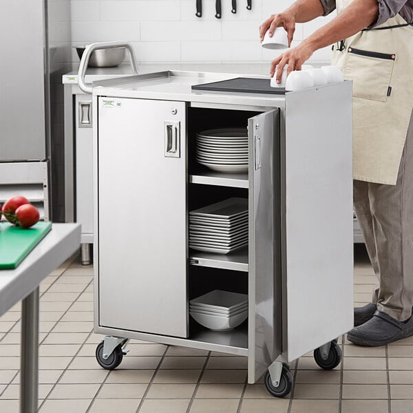 A man using a Regency stainless steel utility cart with enclosed shelves to transport plates.