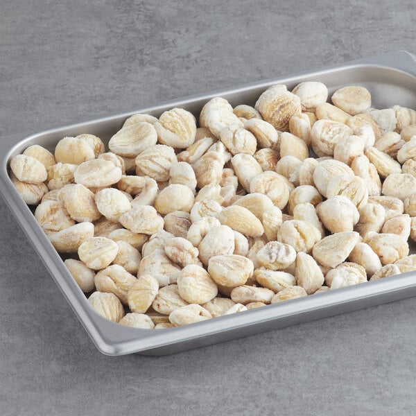 A metal pan filled with White Toque raw peeled chestnuts on a gray surface.