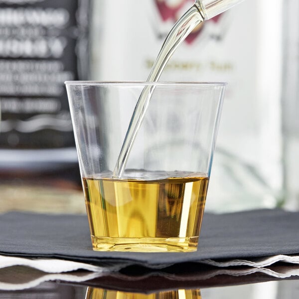A person pouring whiskey into a Fineline Quenchers plastic shot cup on a table in a bar.